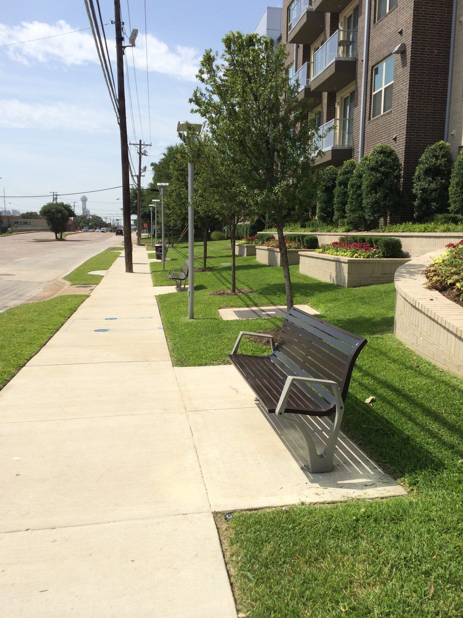 A sidewalk with a row of benches along a street in front of an apartment building.
